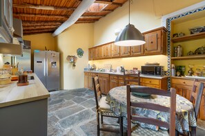 Una cocina con armarios de madera, suelo de piedra, una mesa de comedor con sillas y una lámpara colgante.