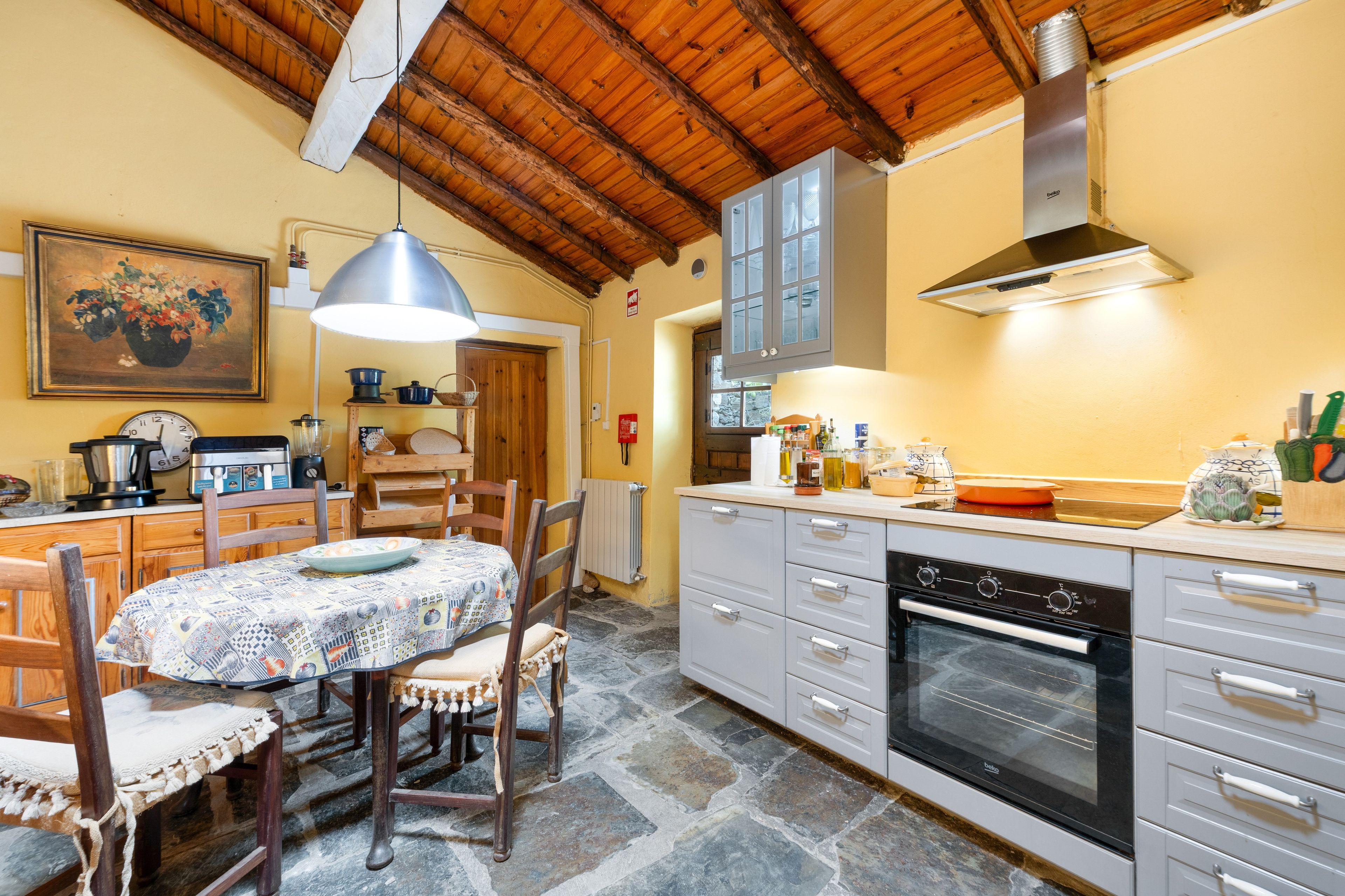 Una cocina con piso de piedra, armarios de madera, una estufa y una mesa de comedor con sillas.