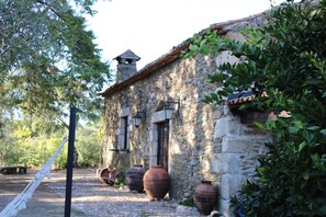 A rustic stone building with a tiled roof, large clay pots, and a hammock.