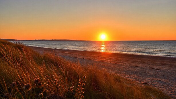 Una spiaggia al tramonto, con il sole che si riflette sull'acqua.
