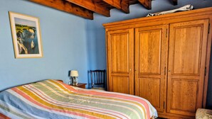 Una camera da letto con un letto, un'armadio in legno, una sedia, un comodino e un quadro appeso al muro.