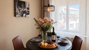 Un comedor con una mesa redonda, sillas, un jarrón con flores, una botella de vino y una fotografía blanco y negro en la pared.