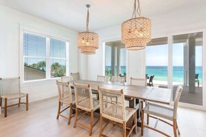 A dining area with a large table, wicker chairs, and two hanging light fixtures. - Gulf-Front Luxury Home with Private Pool, Beach Access & Bikes! (Panama City Beach)