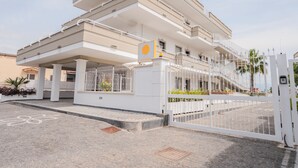 Un edificio de varios pisos con una entrada porticada, un cartel que indica una zona de estacionamiento 70A y una palmera al fondo.