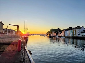 Blick auf das Wasser mit Gebäuden, einem Steg und einem Sonnenuntergang.