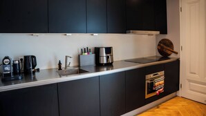 Une cuisine moderne avec des meubles noirs, un plan de travail en acier inoxydable, une machine à café et un four encastré.