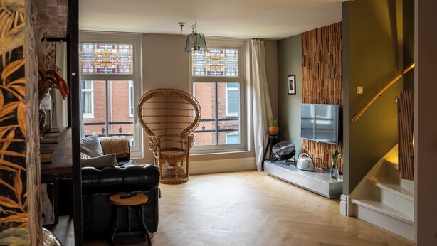 Un salon moderne avec un canapé, un fauteuil en osier, un téléviseur et un escalier.