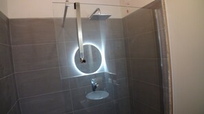 Ein modernes Badezimmer mit einer gläsernen Duschkabine, einer runden Leuchte und einem Handtrockner.