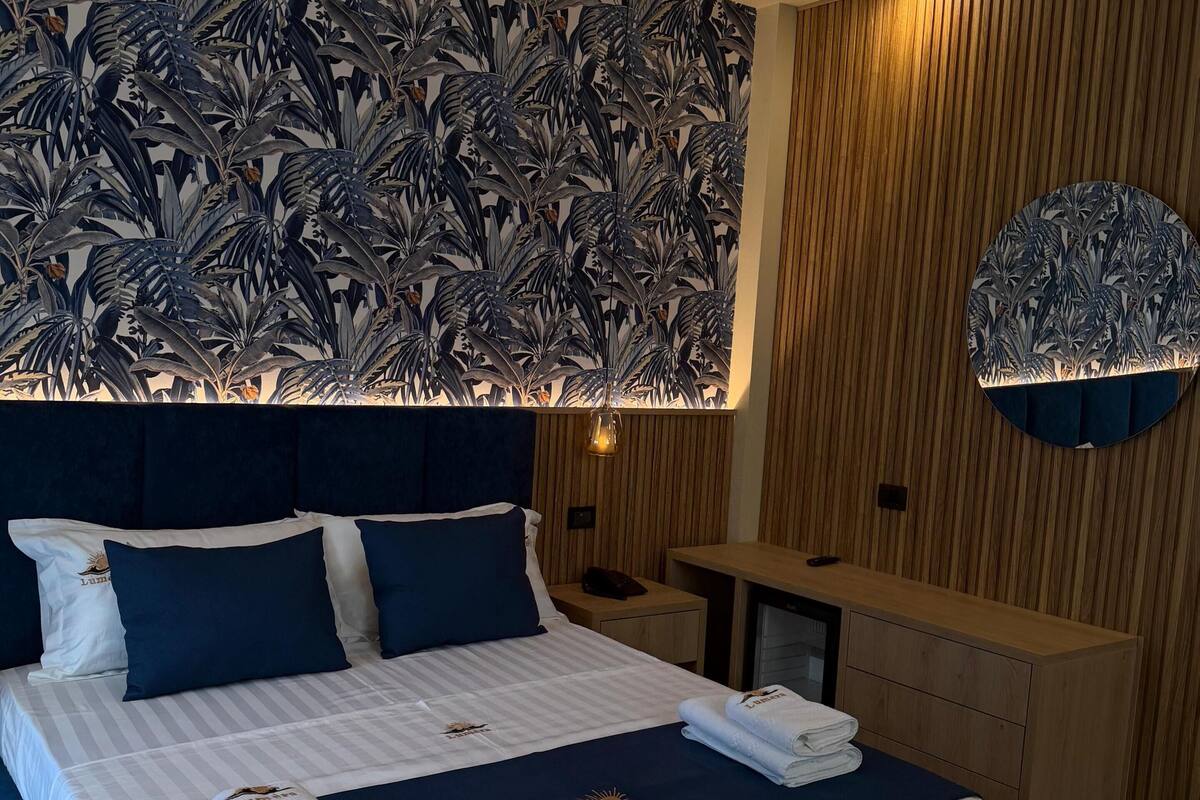 A hotel room with a large bed, a wooden headboard, a wall-mounted light fixture, and a small desk.