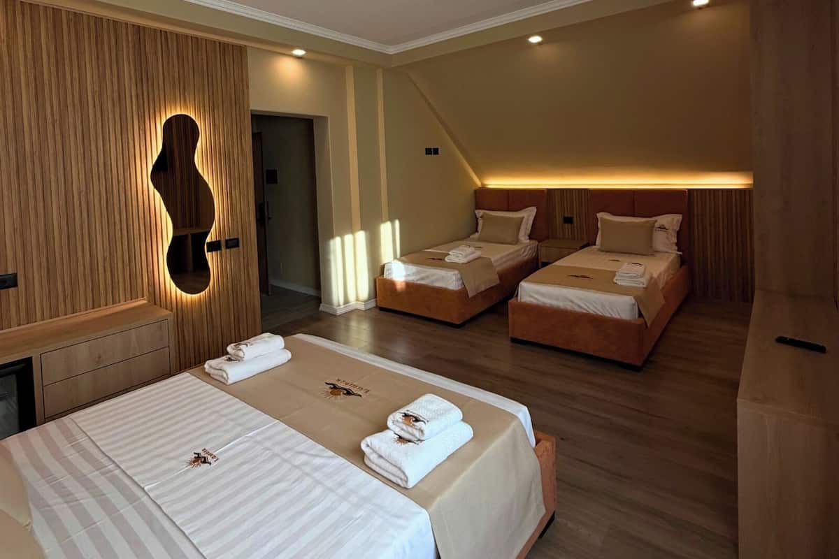 A hotel room with two beds, a wooden wall with a circular mirror, and a ceiling light.