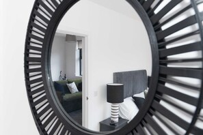 A circular mirror reflecting a room with a bed, a nightstand, a lamp, and a green sofa.