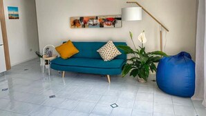 Un salon moderne avec un canapé turquoise, un pouf bleu, une lampe sur pied et un tableau accroché au mur.