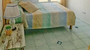 Une chambre à coucher avec un lit, une table de chevet avec une lampe, un tableau encadré au mur et une fenêtre donnant sur un paysage.