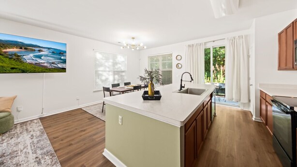 A modern kitchen with a central island, wooden cabinets, and a large window. - Rocking Oak Cottage of Charleston (Summerville)