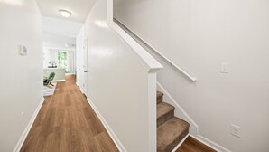 A clean, modern hallway with wooden flooring, white walls, and a carpeted staircase. - Rocking Oak Cottage of Charleston (Summerville)