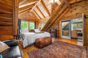 A wooden cabin bedroom with a bed, a sofa, a rug, and a sliding door to a balcony. - Salty Pines- Guest Favorite (Lake Lure)