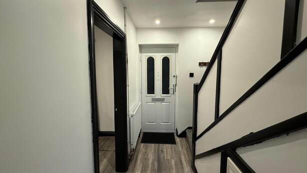 A hallway with a white door, black-framed staircase, and a wooden floor. - Rest and Recover (West Bromwich)