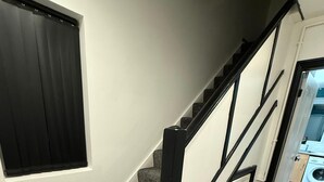 A staircase with carpeted steps and a black railing, leading to a room with a window and a view of a laundry area. - Rest and Recover (West Bromwich)