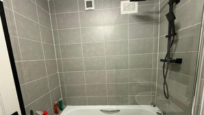 A bathroom with a bathtub, shower, and tiled walls. - Rest and Recover (West Bromwich)