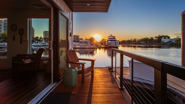 Un balcón con vista al atardecer sobre un puerto deportivo, una silla y una mesita.