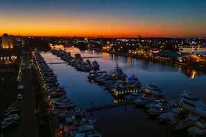 A marina at dusk with boats docked, a calm water body, and city lights in the background.