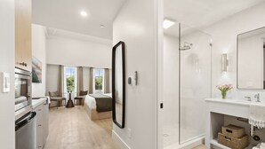 A modern hotel room with a kitchenette, a glass-enclosed shower, a large mirror, and a view of the outdoors. - Casa Iglesia Studio 304 (Santa Barbara)