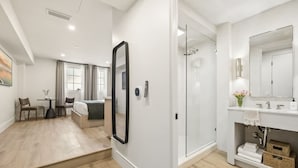 Habitació d'hotel moderna amb zona d'estar independent, un mirall gran, dutxa i tocador blanc.
