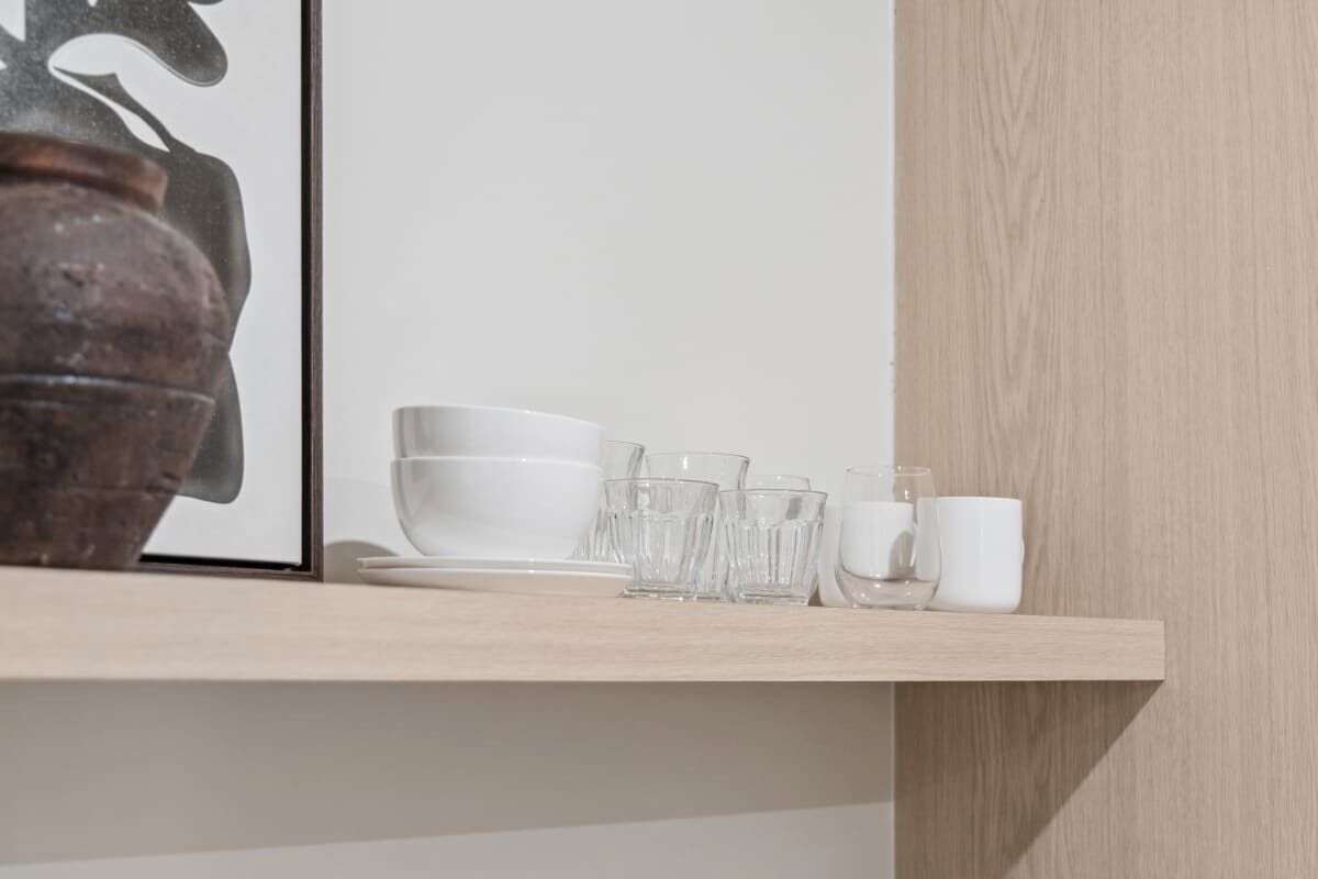En træhylde med hvide skåle, glas og en kop.