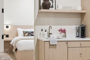 Ein Hotelzimmer mit einem Bett, einem weißen Waschbecken, einer Kaffeemaschine und einem Regal mit Tassen und einer Vase.
