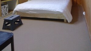 Un dormitorio con techo de madera, una cama con edredón blanco, un taburete pequeño y una mesita de noche con una lámpara.