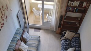 Una habitación pequeña con sofá, cama, una mesita y una estantería.