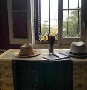 A room with a window, a chair, and two hats on a table.