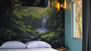 Un dormitorio con cama, almohadas, mesita de noche, panel de control en la pared y ventana con cortinas.