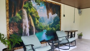 Una habitación con un gran mural de una cascada y bosque, dos sillones con cojines, una mesita y una planta en maceta.