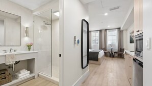A modern hotel room with a shower, a large mirror, a bed, a dining area, and a kitchen. - Casa Iglesia Studio 104 (Santa Barbara)