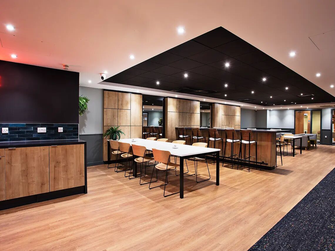 A modern conference room with wooden tables and chairs, a black ceiling, and a visible plant.