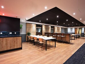 A modern conference room with wooden tables and chairs, a black ceiling, and a visible plant. - For Students Only - The Curve in London (London)