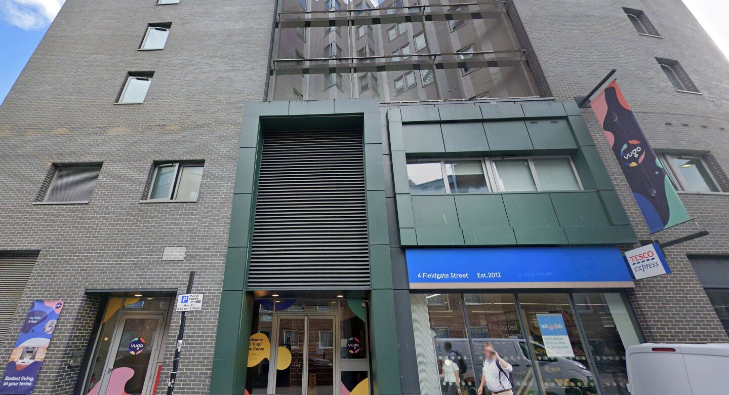 A building with a modern facade, a Tesco Express store, and a sign for a parking area.
