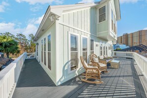 A coastal house with a wooden deck, rocking chairs, and a white railing.