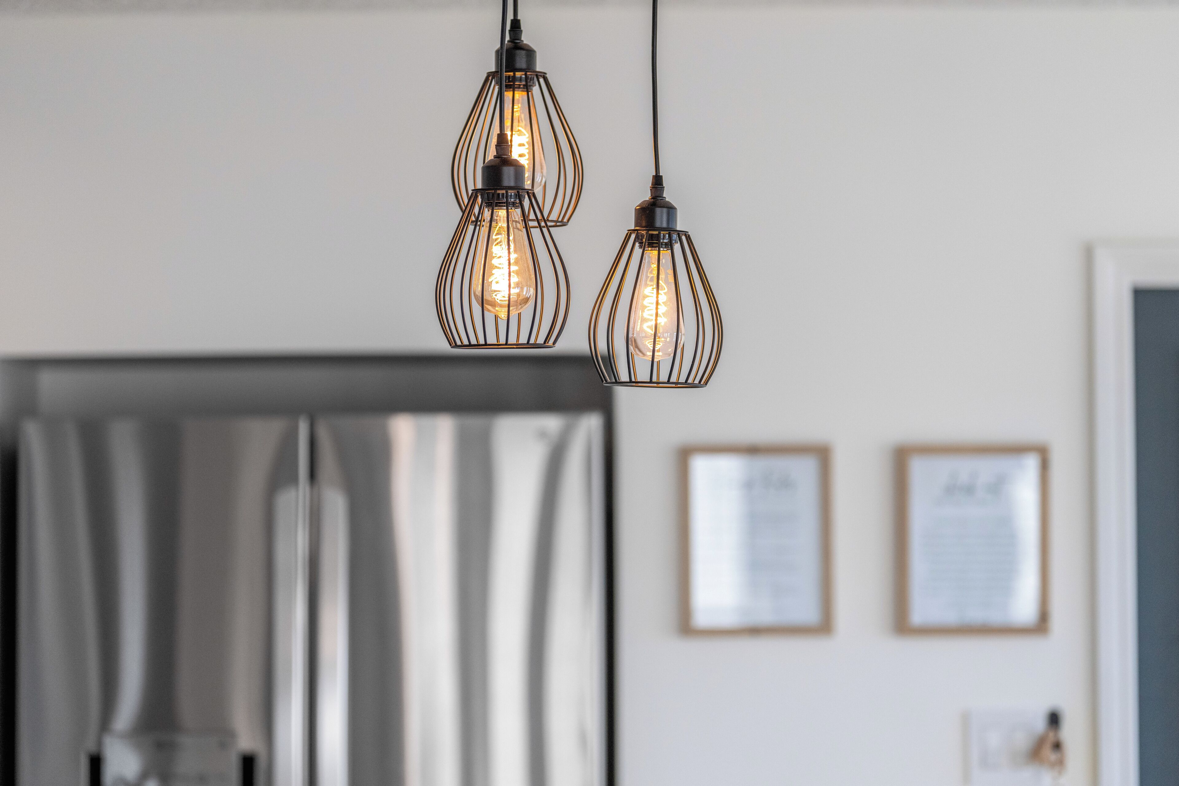 A kitchen with three hanging pendant lights, stainless steel appliances, and framed certificates on the wall.