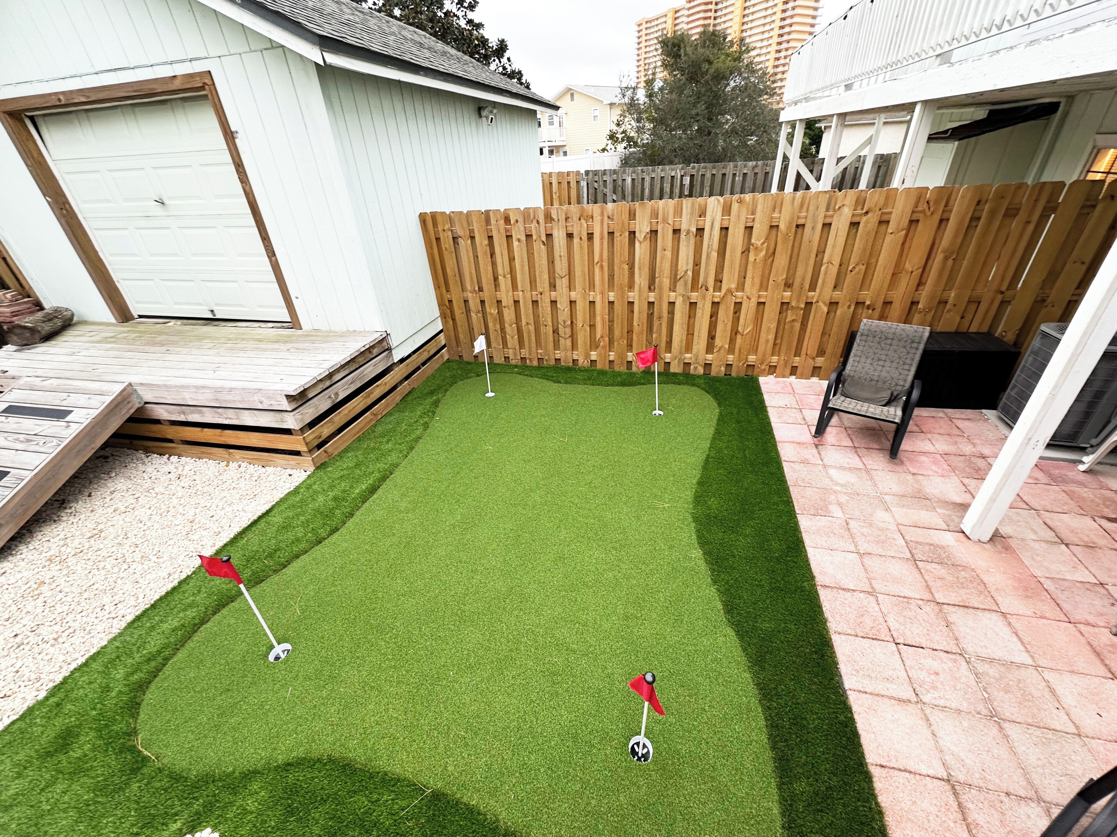 Een achtertuin met kunstgras, een houten terras en een houten schutting.