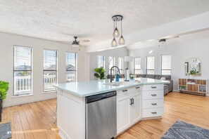 A modern kitchen with a dishwasher, white cabinetry, and a large island.
