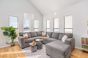 Ein modernes Wohnzimmer mit einer Eckcouch, runden Couchtischen und einer großen Topfpflanze.