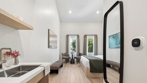 Ein Hotelzimmer mit Küchenzeile, einer Sitzecke mit einer Bank, einem Bett, einem großen Spiegel und einem Thermostat.
