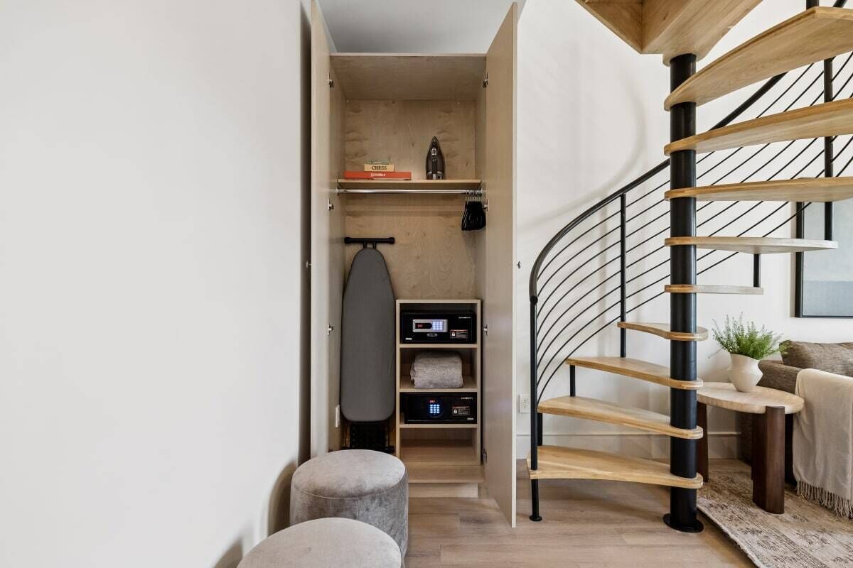 A modern interior with a spiral staircase, a small seating area, and a compact storage unit with a digital device.