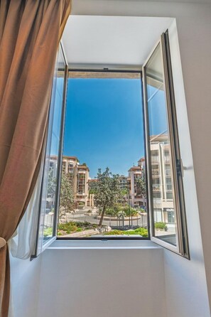 A window with a view of a residential area, including buildings and greenery. - Luxe Port de Nice - 3P Neuf - Balnéo double (Nice)
