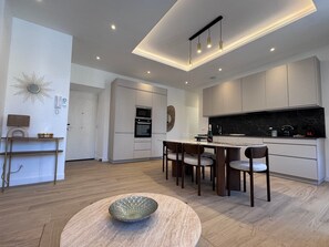 A modern kitchen with a central island, built-in oven, and a dining area with chairs. - Luxe Port de Nice - 3P Neuf - Balnéo double (Nice)