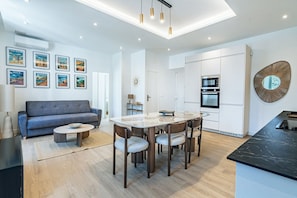 A modern kitchen with a built-in oven, a dining area with a marble table, and a living room with a sofa and wall art. - Luxe Port de Nice - 3P Neuf - Balnéo double (Nice)