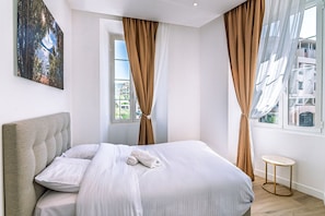 A bedroom with a bed, curtains, a round table, and a painting on the wall. - Luxe Port de Nice - 3P Neuf - Balnéo double (Nice)