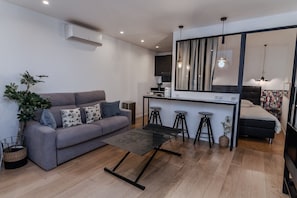 En moderne stue med en grå sofa, et sort sofabord og et køkkenområde med barstole.